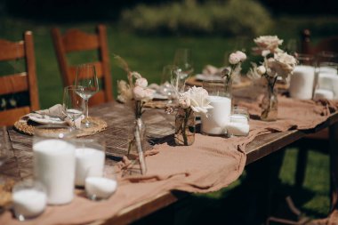 Koyu ahşap bir masa, bej bir koşucu, beyaz tabaklar ve basit çiçek süslemeleri olan kırsal bir açık hava düğün masası.
