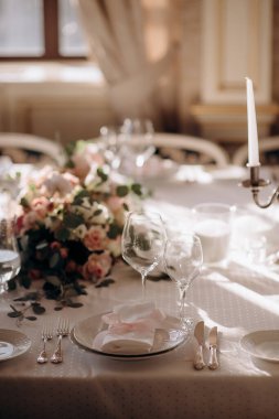 Beyaz masa örtüsü, pembe peçeteler, basit bir çiçek süsü ve gümüş tutacağında uzun beyaz bir mum olan zarif bir düğün masası.