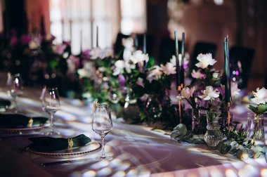 Beyaz masa örtüsü, koyu yeşil peçeteler, altın çerçeveli tabaklar ve basit beyaz çiçek dekoru olan zarif bir düğün masası.