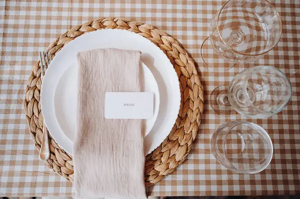 Açık kahverengi keten peçetede gelin kartı olan zarif bir düğün yerinin yukarıdan aşağıya yakın çekimi.