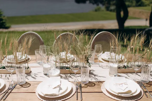 Kurumuş çiçekler, dokuma kaplar ve doğal ahşap elementlerle süslü zarif bir açık hava masası.