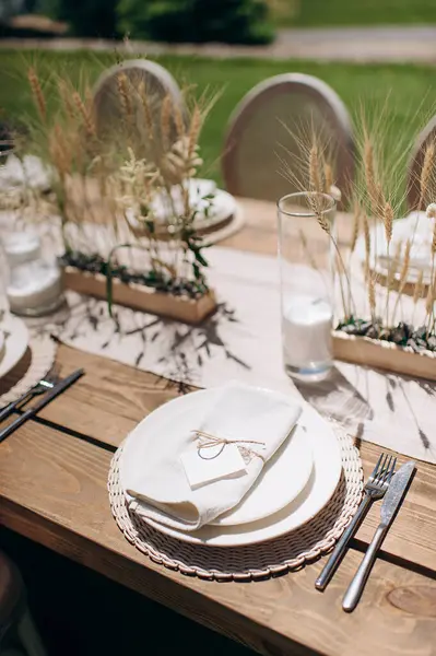 Kurumuş çiçekler, dokuma kaplar ve doğal ahşap elementlerle süslü zarif bir açık hava masası.