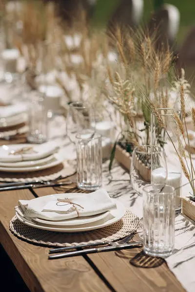 Kurumuş çiçekler, dokuma kaplar ve doğal ahşap elementlerle süslü zarif bir açık hava masası.