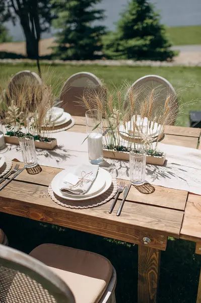 Kurumuş çiçekler, dokuma kaplar ve doğal ahşap elementlerle süslü zarif bir açık hava masası.