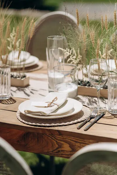 Kurumuş çiçekler, dokuma kaplar ve doğal ahşap elementlerle süslü zarif bir açık hava masası.