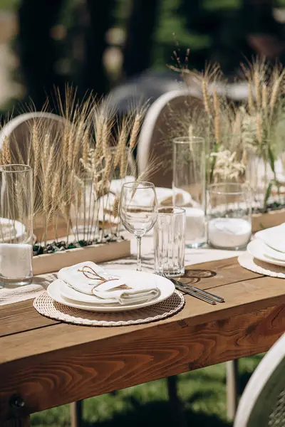 Kurumuş çiçekler, dokuma kaplar ve doğal ahşap elementlerle süslü zarif bir açık hava masası.