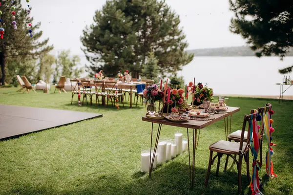 Açık havada, ahşap bir masası, renkli çiçekleri ve sandalye süslemeleri olan bir başkanlık.