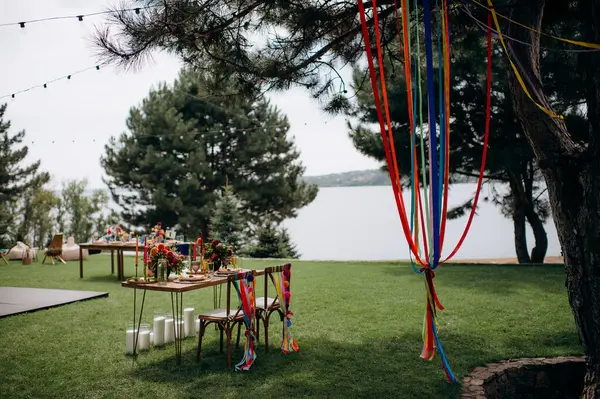 Açık havada, ahşap bir masası, renkli çiçekleri ve sandalye süslemeleri olan bir başkanlık.