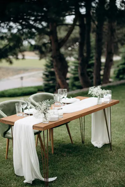 Ahşap bir masası, beyaz bir koşucusu ve narin çiçek aksanıyla şık bir açık hava düğün başkanlığı.