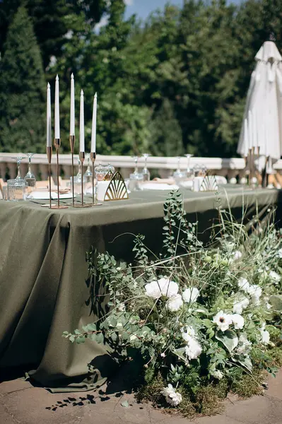 Zeytin yeşili masa örtüsü, beyaz tabaklar ve altın mum tutacağı olan zarif açık hava düğün başkanlığı.
