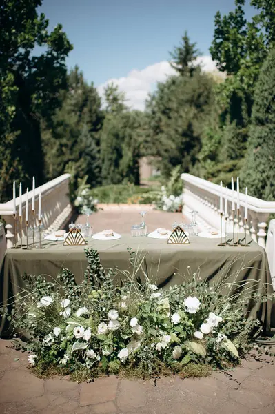 Zeytin yeşili masa örtüsü, beyaz tabaklar ve altın mum tutacağı olan zarif açık hava düğün başkanlığı.