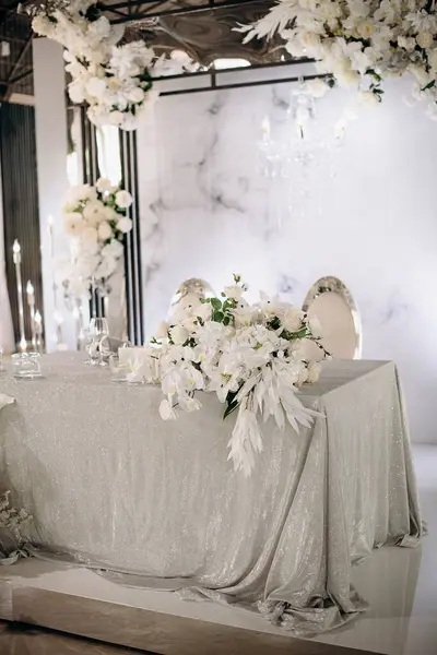 Işıldayan gümüş masa örtüsü ve yemyeşil beyaz çiçek düzenlemeleri olan şık bir iç mekan düğün başkanlığı.