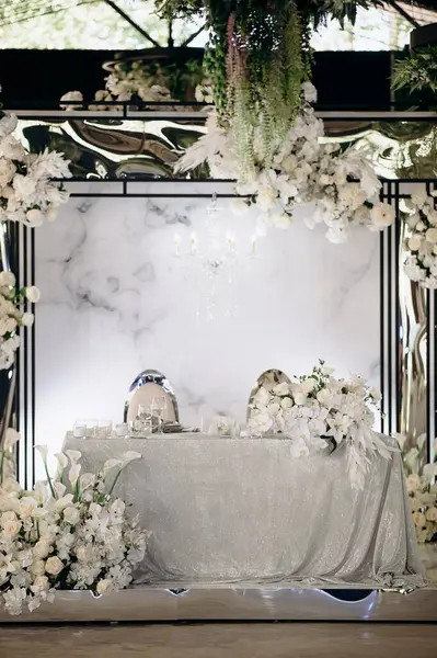 Işıldayan gümüş masa örtüsü ve yemyeşil beyaz çiçek düzenlemeleri olan şık bir iç mekan düğün başkanlığı.
