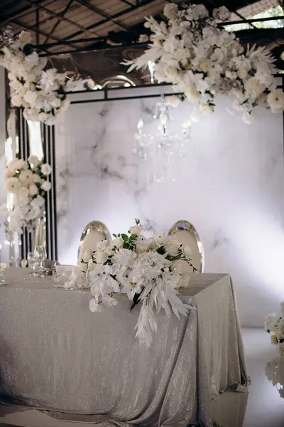 Işıldayan gümüş masa örtüsü ve yemyeşil beyaz çiçek düzenlemeleri olan şık bir iç mekan düğün başkanlığı.