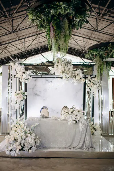 Işıldayan gümüş masa örtüsü ve yemyeşil beyaz çiçek düzenlemeleri olan şık bir iç mekan düğün başkanlığı.