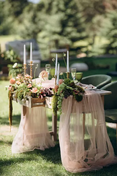 Ahşap bir masası, şeftali tülü koşucusu, yosun, sulu mumları olan taşralı açık hava düğün başkanlığı.