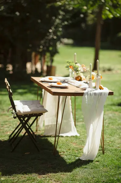 Tahta bir masası, beyaz koşucusu, turuncu çiçekli aksanı ve yeşil çimi olan şık bir açık hava düğün başkanı.