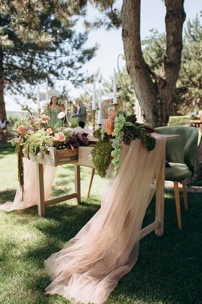 Ahşap bir masası, şeftali tülü koşucusu, yosun, sulu mumları olan taşralı açık hava düğün başkanlığı.