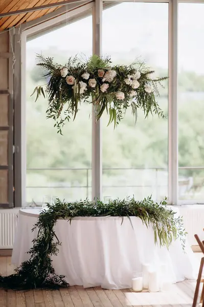 Beyaz örtülü bir masa örtüsü ve beyaz çiçekli yemyeşil bir çelengi olan şık, kapalı bir düğün başkanlığı.