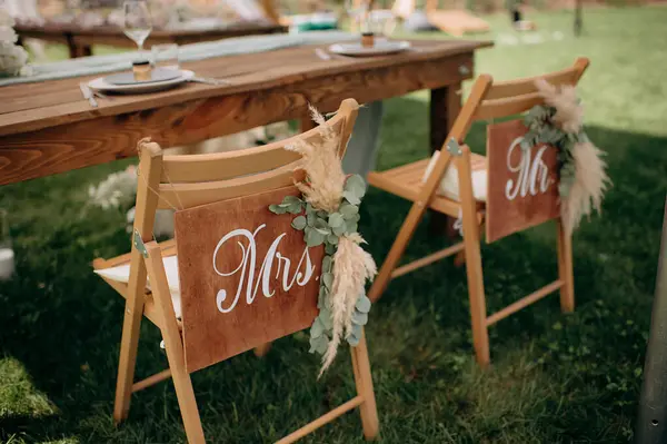 Bay ve Bayan tabelaları ve otlarla süslenmiş ahşap sandalyeli kırsal açık hava düğün başkanlığı.