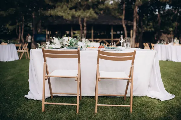Beyaz masa örtüsü ve yeşil çimlerin üzerinde çiçek aranjmanları olan zarif bir açık hava düğün başkanlığı.