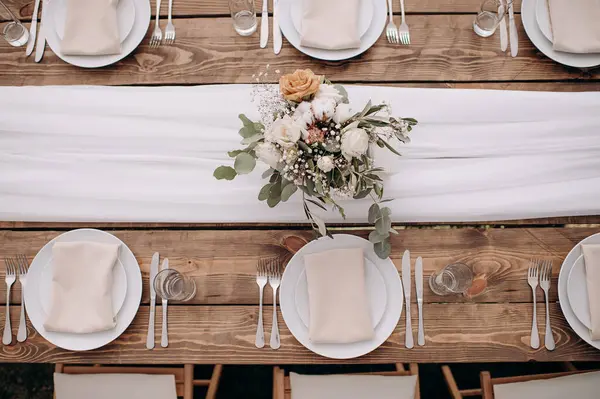 Üzerinde ahşap bir masa, beyaz bir koşucu, beyaz plaka ve çiçek desenli bir düğün masası manzarası var.