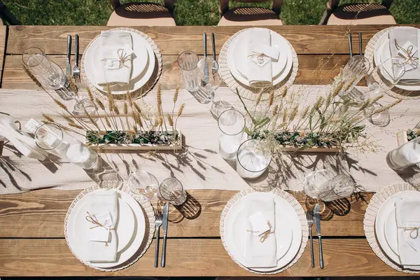 Ahşap bir masa, beyaz bir koşucu, basit çiçek aksanlı ve beyaz plakalı kırsal bir düğün masası manzarası.