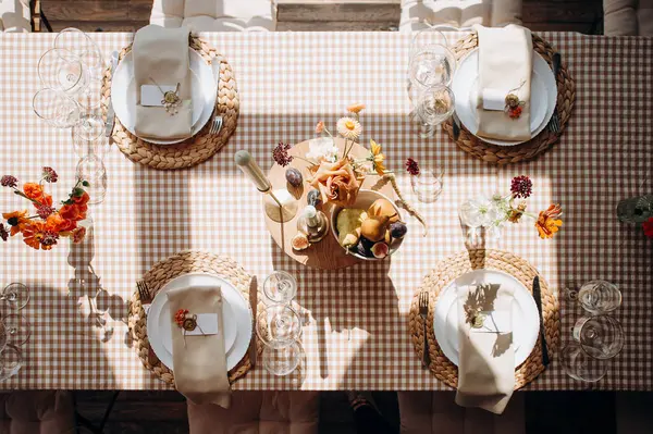 Kırsal bir düğün masası manzarası, kareli bir masa örtüsü, dokunmuş kaplar, beyaz tabaklar ve meyve dekoru.