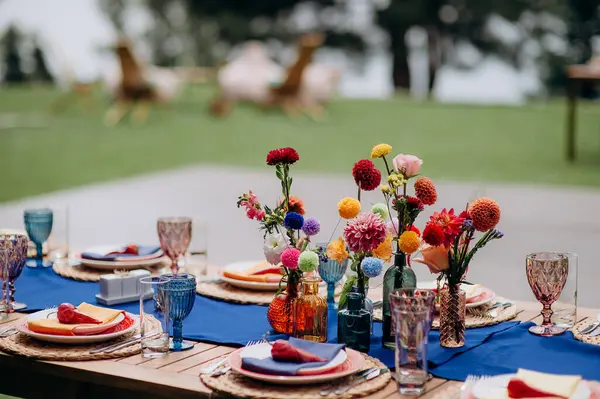 Mavi bir koşucu, dokuma tabaklar, pembe tabaklar ve renkli çiçek süslemeleri olan şık bir açık hava düğün masası.