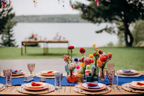 Mavi bir koşucu, dokuma tabaklar, pembe tabaklar ve renkli çiçek süslemeleri olan şık bir açık hava düğün masası.