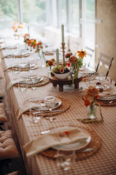 Kareli masa örtüsü, dokuma kapları, basit çiçek dekoru ve meyve aksanıyla şık bir açık hava düğün masası.