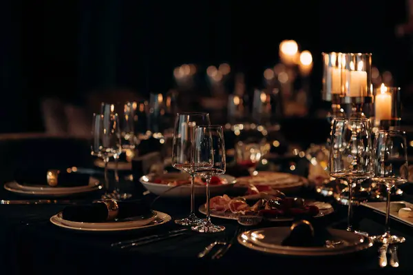 Siyah masa örtüsü, altın çerçeveli tabaklar, koyu peçeteler ve yanan mumlarla dolu gümüş bir şamdan.