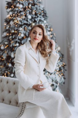Genç Avrupalı mutlu iş kadını arkasında süslü bir Noel ağacı olan bir fincan kahveyle, kış tatillerinde ev ofisinde çalışan bir kadın. Yumuşak seçici odak.