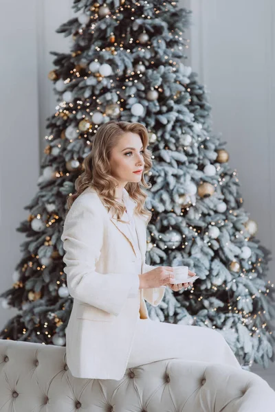 クリスマスツリーの後ろに装飾されたコーヒーのカップを持つ若い幸せなヨーロッパの実業家 冬の休暇中に自宅のオフィスで働く女性 柔らかい選択的フォーカス — ストック写真