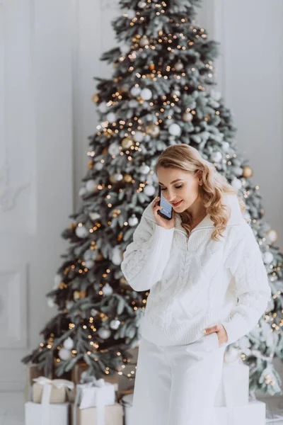 クリスマスツリーの後ろに飾られた職場でクライアントと携帯電話で話す幸せなヨーロッパの実業家 冬休み中に自宅のオフィスで働く笑顔の女性 柔らかい選択的フォーカス — ストック写真