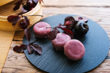 Mor toplarla süslenmiş siyah bir tabak ve kırsal ahşap bir masada sergilenen yapraklar zarif ve şık bir yemek sunumu yaratıyor. Mochi Asya tatlısı.