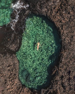 Woman swimming in a clear sea lagoon in Fuerteventura drone shot