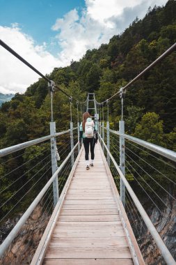 Mutlu kız sırt çantalı dağlarda ve ormanlarda köprüde yürüyüş yapıyor.