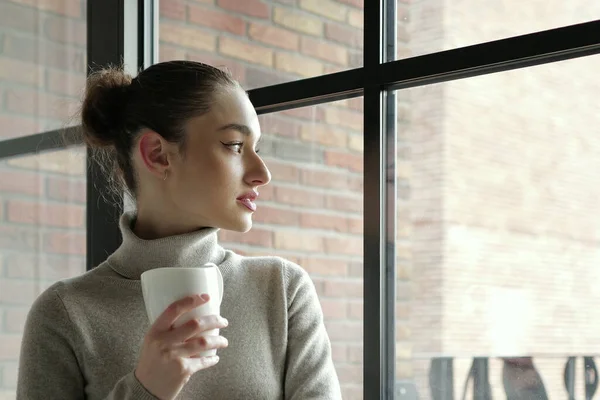 woman with a cup of coffee looking in the window