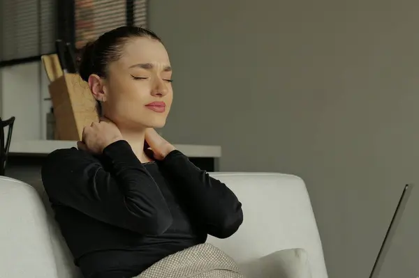Portrait of a young woman with a neck pain rubbing massaging tensed muscles after long computer work study in incorrect posture