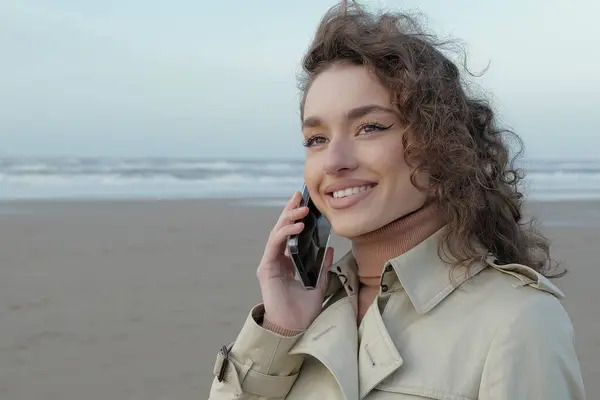 美しい若い笑顔の女性が海と空のビーチで携帯電話で話しています — ストック写真