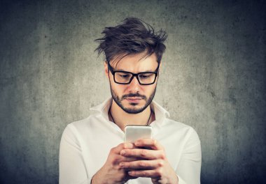 Ciddi bir genç adam cep telefonundan haber okuyor. 