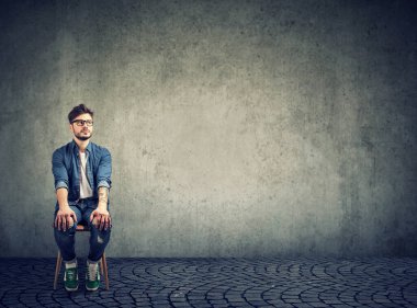 Duvarın yanındaki sandalyede oturan bir adam endişeyle röportaj için bekliyor. 