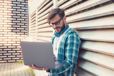 Güneşli bir günde dışarıda dikilirken dizüstü bilgisayarını kullanan mutlu hippi.
