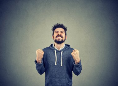 Neşeli genç adam başarıyı yumruklarıyla kutluyor izole gri duvar arkaplanıyla