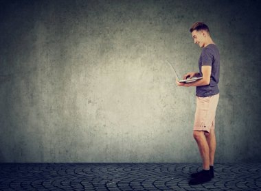 Duvarın yanında duran bir adam dizüstü bilgisayar kullanıyor.