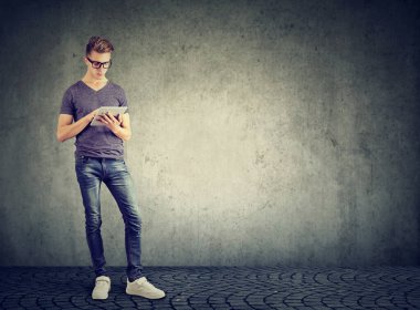 Duvarın yanında durup tablet bilgisayarını kullanan sıradan bir adam. 