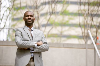 Kendine güvenen, şık bir takım elbiseli siyahi işadamı kollarını kavuşturmuş kameraya bakıyor. 