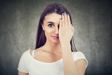 Bir kadın kameraya bakarken bir gözünü eliyle kapatıyor.