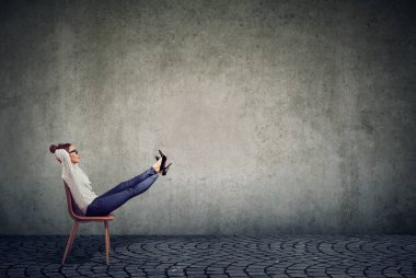 Ofis sandalyesinde oturan genç iş kadını bacaklarını kaldırmış hayal kuruyor. 